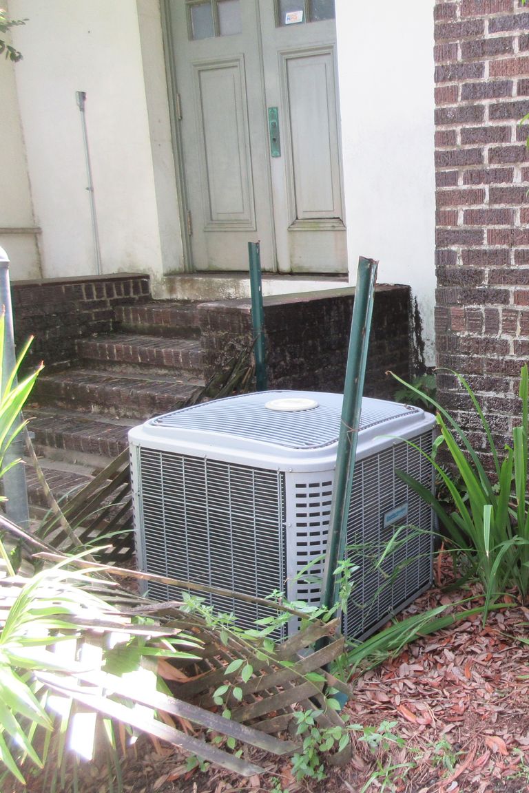 A central air conditioner condenser beside brick steps, with a gas meter and garden plants