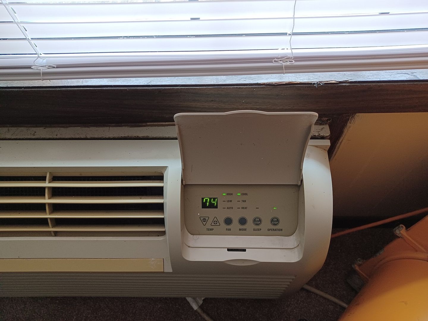 A through-wall packaged terminal air conditioner with its control panel open under a window
