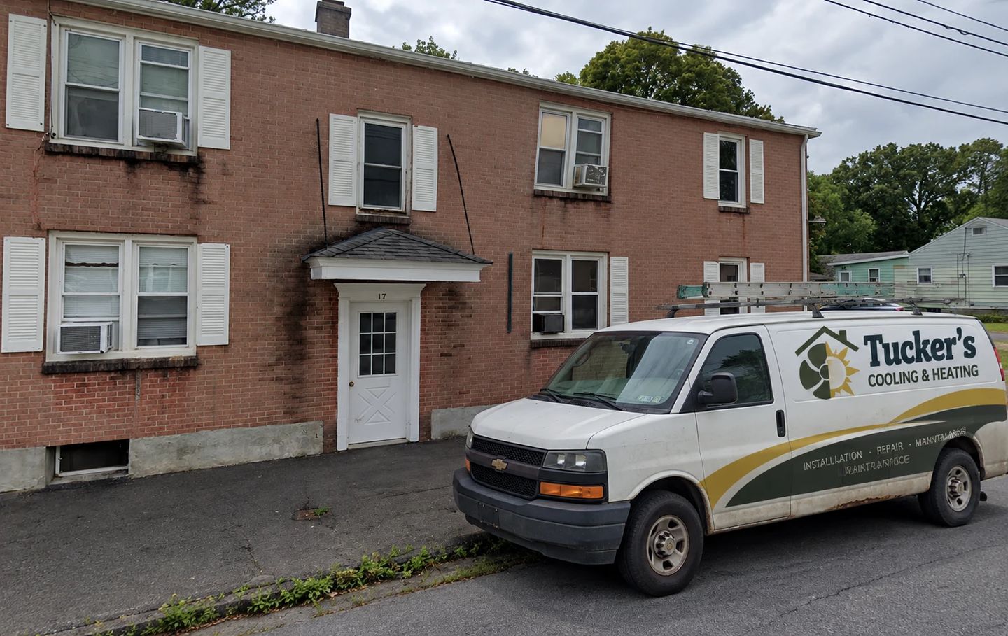 Tucker&rsquo;s Cooling & Heating service van parked outside a brick apartment building in Rensselaer